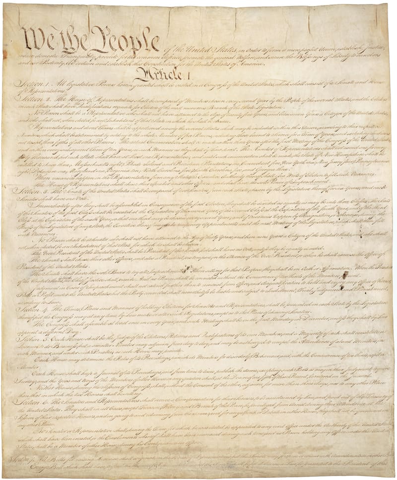 Aged parchment page of the US Constitution with the large handwritten words We the People