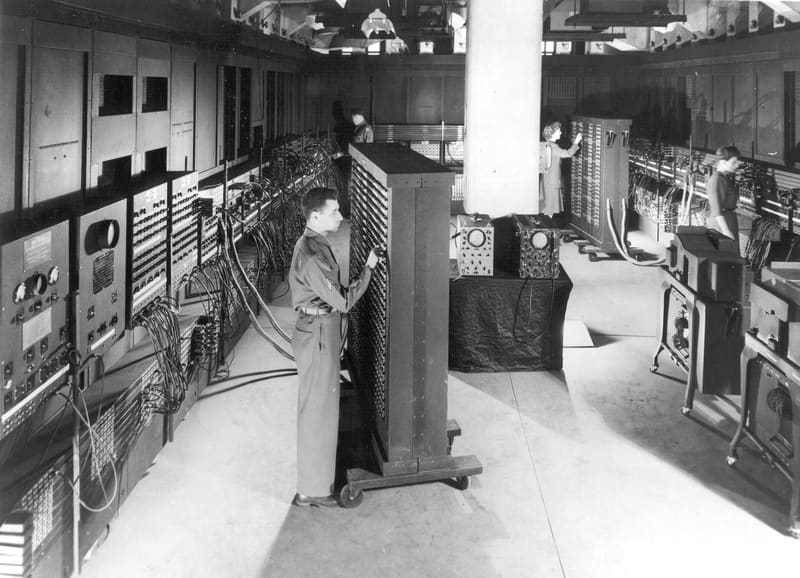 Two operators setting switches and cables on the tall panels of the ENIAC computer