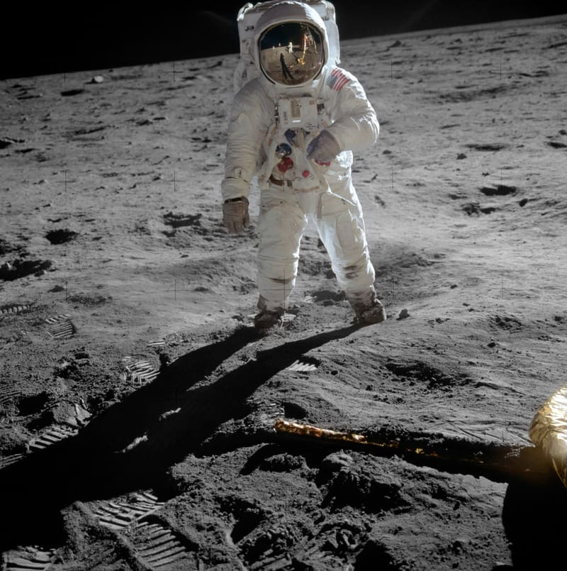 An astronaut in a white spacesuit standing on the grey surface of the Moon