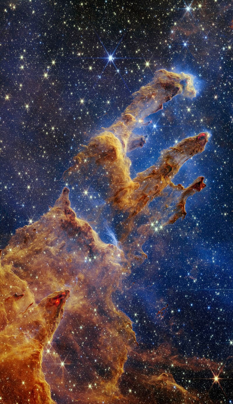 Towering columns of orange and brown gas and dust with bright stars against a dark background